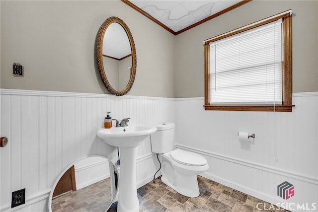 bathroom featuring wainscoting, a sink, stone finish flooring, crown molding, and toilet