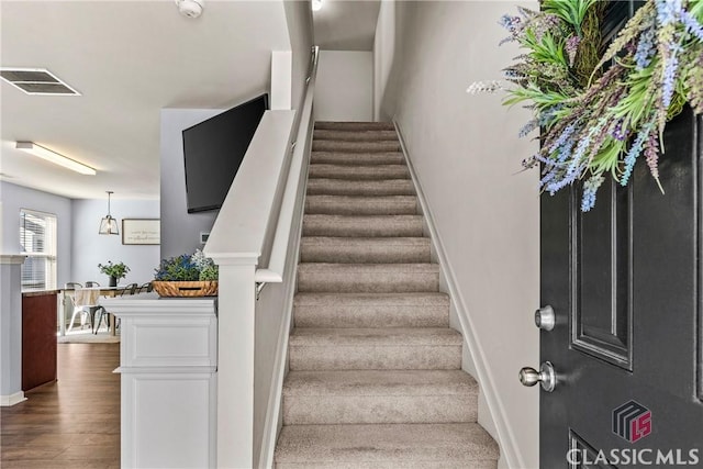 stairway featuring visible vents, baseboards, and wood finished floors