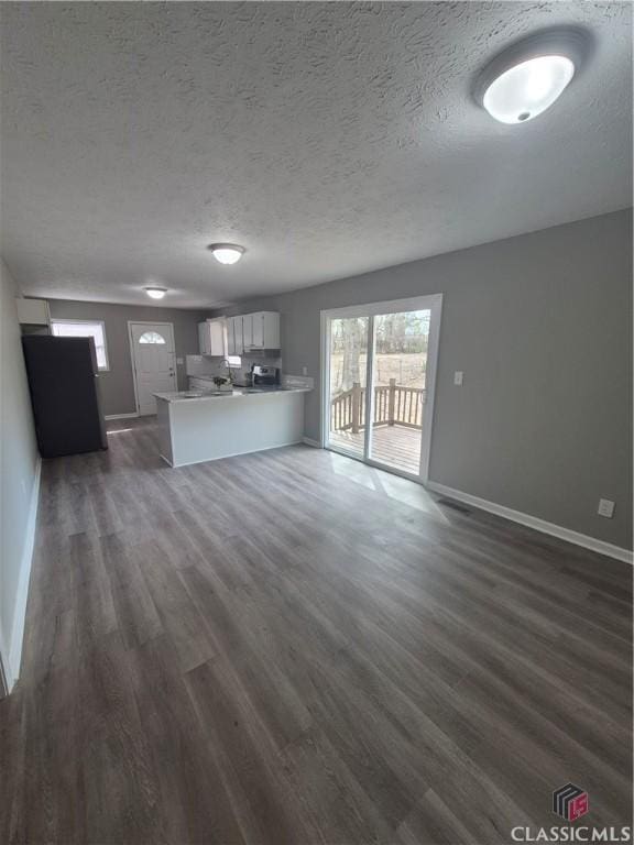 unfurnished living room featuring baseboards, dark wood-style flooring, and a textured ceiling