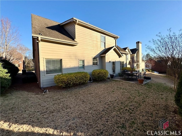 back of property with a lawn, roof with shingles, and a patio area