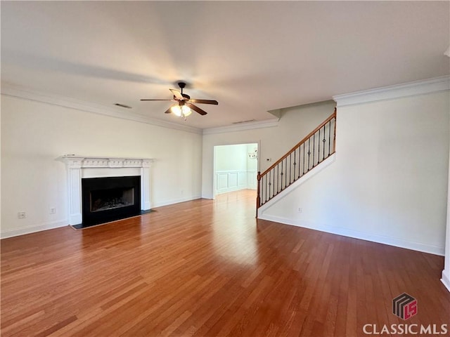 unfurnished living room with visible vents, crown molding, a fireplace with flush hearth, stairs, and wood finished floors