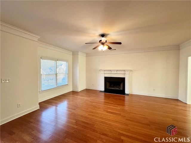 unfurnished living room with baseboards, a fireplace with flush hearth, ornamental molding, wood finished floors, and a ceiling fan