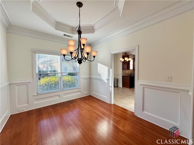 unfurnished dining area with a raised ceiling, hardwood / wood-style flooring, visible vents, and a chandelier