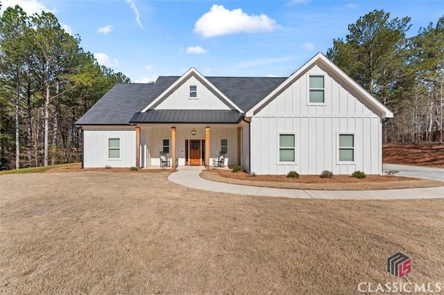 modern inspired farmhouse with a standing seam roof, a porch, board and batten siding, a front yard, and metal roof