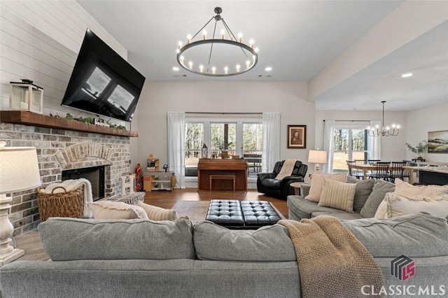 living room with a chandelier, recessed lighting, a brick fireplace, and wood finished floors