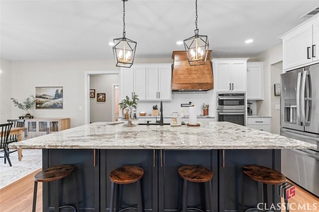 kitchen with visible vents, stainless steel appliances, light wood-style floors, white cabinets, and custom exhaust hood