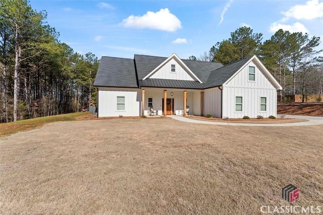 modern farmhouse with board and batten siding, a front lawn, covered porch, metal roof, and a standing seam roof