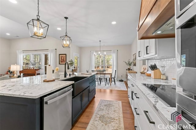 kitchen featuring wood finished floors, light stone countertops, stainless steel appliances, white cabinetry, and exhaust hood