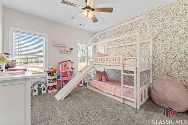 carpeted bedroom featuring wallpapered walls, a ceiling fan, and visible vents