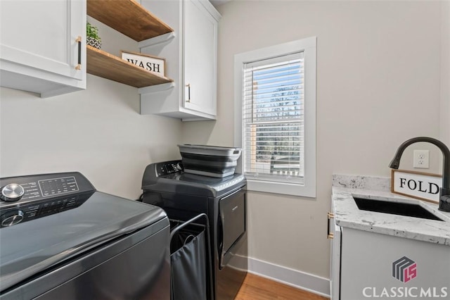 laundry area with baseboards, light wood-style flooring, separate washer and dryer, cabinet space, and a sink