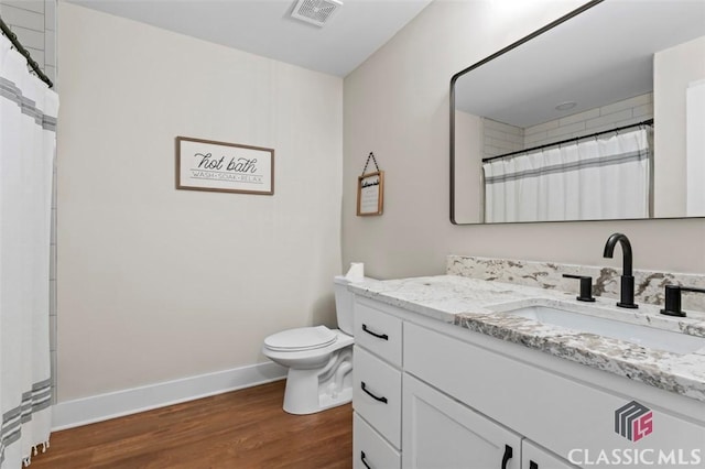 bathroom featuring visible vents, baseboards, toilet, wood finished floors, and vanity