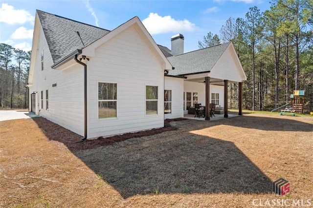 rear view of house featuring a playground, roof with shingles, a chimney, and a patio area