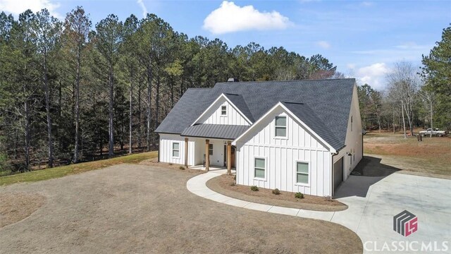 modern farmhouse featuring metal roof, board and batten siding, concrete driveway, and a standing seam roof