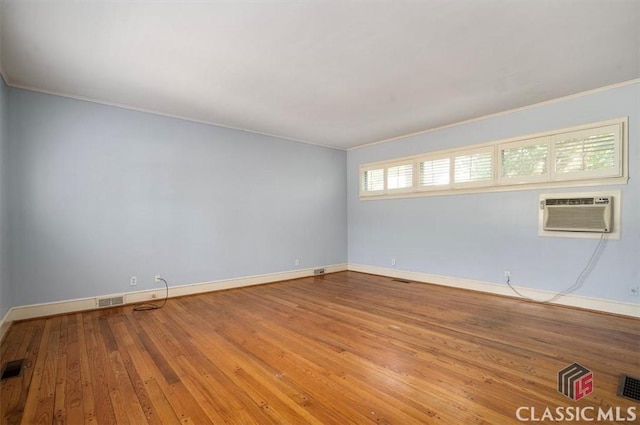 empty room featuring visible vents, crown molding, baseboards, hardwood / wood-style flooring, and a wall mounted AC