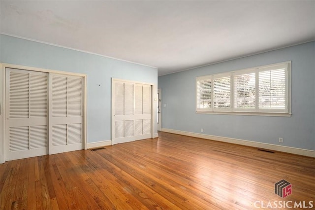 unfurnished bedroom with visible vents, baseboards, two closets, and wood finished floors