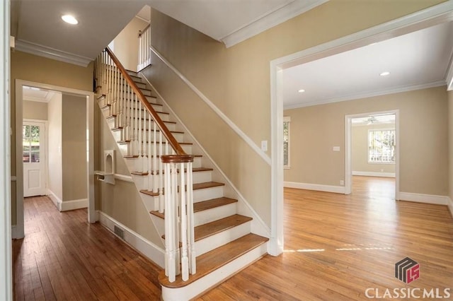 staircase featuring baseboards, a healthy amount of sunlight, wood finished floors, and crown molding