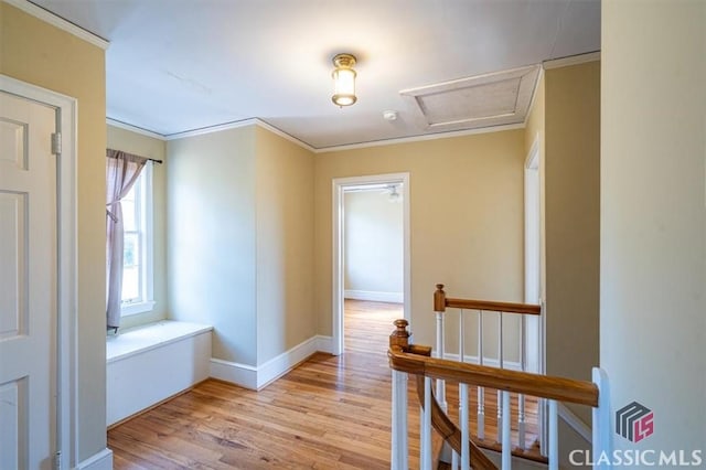 hallway featuring an upstairs landing, crown molding, light wood finished floors, baseboards, and attic access