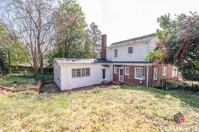 back of house featuring a lawn, fence, a garden, brick siding, and a chimney