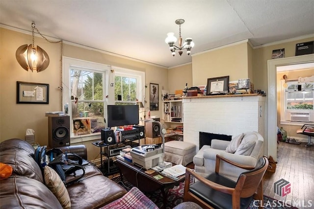 living room featuring a notable chandelier, cooling unit, wood-type flooring, crown molding, and a brick fireplace