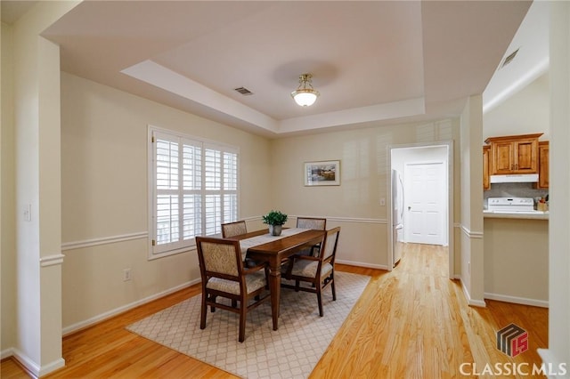 dining area with a raised ceiling, baseboards, light wood-type flooring, and visible vents