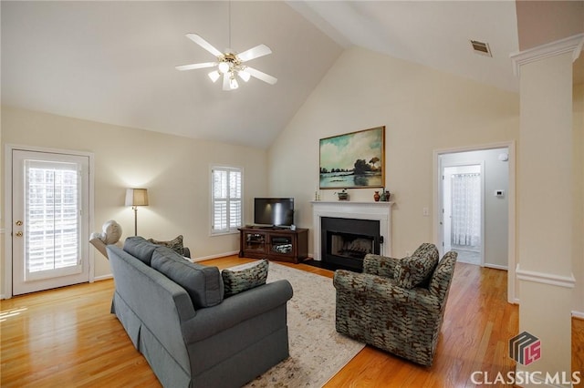 living area with visible vents, light wood finished floors, high vaulted ceiling, a fireplace with flush hearth, and decorative columns