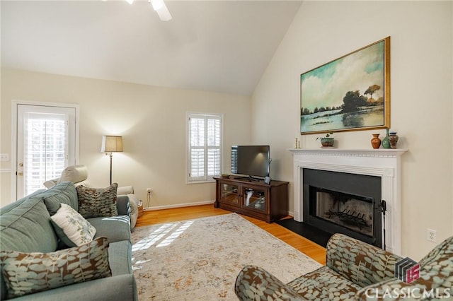 living area with ceiling fan, a fireplace with flush hearth, wood finished floors, and vaulted ceiling