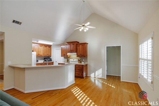 kitchen featuring white appliances, a peninsula, light countertops, under cabinet range hood, and light wood-type flooring