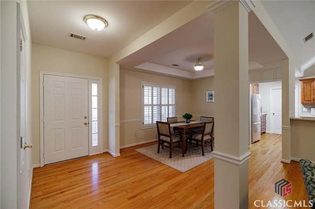 entryway featuring a tray ceiling, baseboards, visible vents, and light wood finished floors