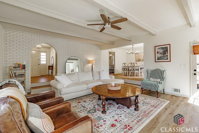 living area featuring visible vents, beamed ceiling, ceiling fan with notable chandelier, wood finished floors, and arched walkways