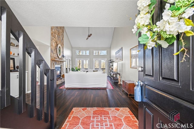 foyer featuring a stone fireplace, a textured ceiling, lofted ceiling, and wood finished floors