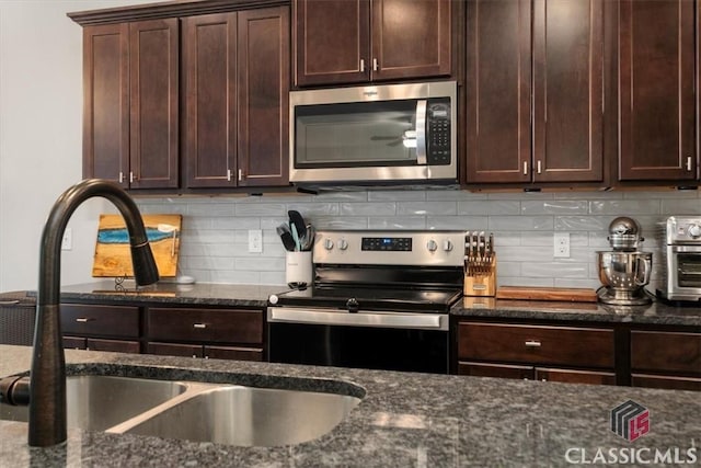 kitchen featuring decorative backsplash, dark stone countertops, stainless steel appliances, and a sink