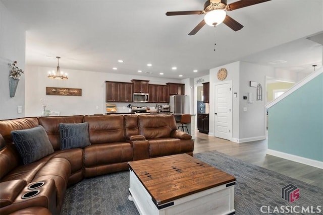 living room with recessed lighting, ceiling fan with notable chandelier, dark wood-type flooring, and baseboards