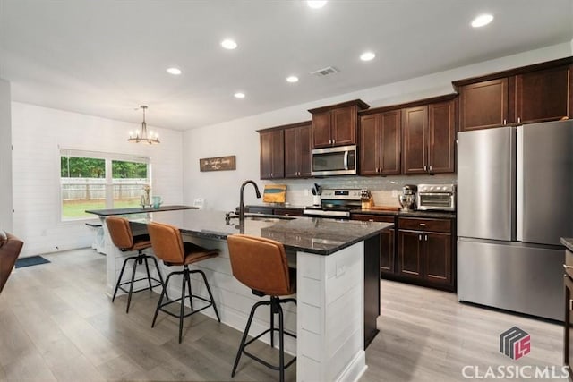 kitchen featuring visible vents, a breakfast bar area, appliances with stainless steel finishes, a notable chandelier, and a sink
