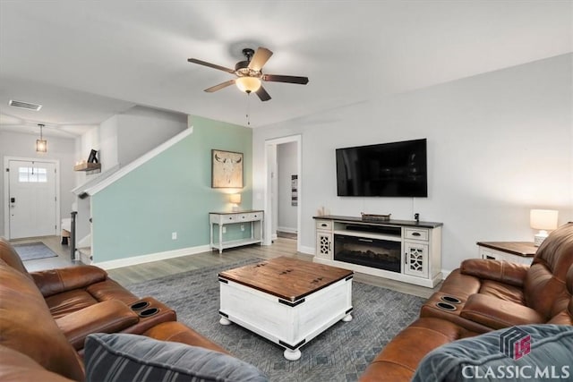 living room featuring visible vents, a ceiling fan, wood finished floors, stairway, and baseboards