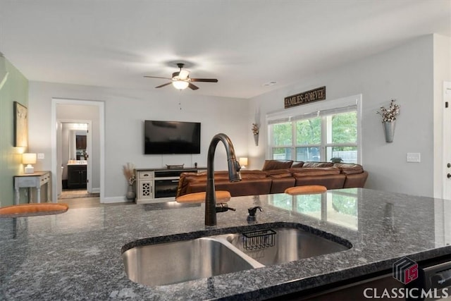 kitchen featuring open floor plan, dark stone counters, ceiling fan, and a sink