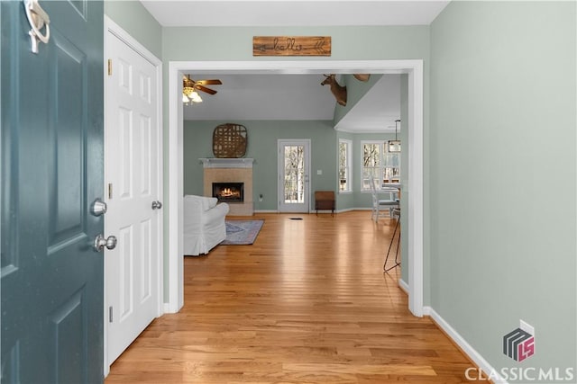 foyer featuring a fireplace, light wood-style floors, baseboards, and ceiling fan