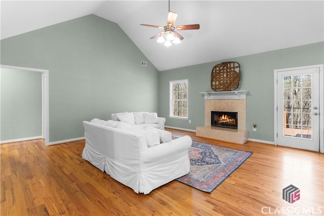 living area featuring a fireplace, baseboards, a ceiling fan, and wood finished floors