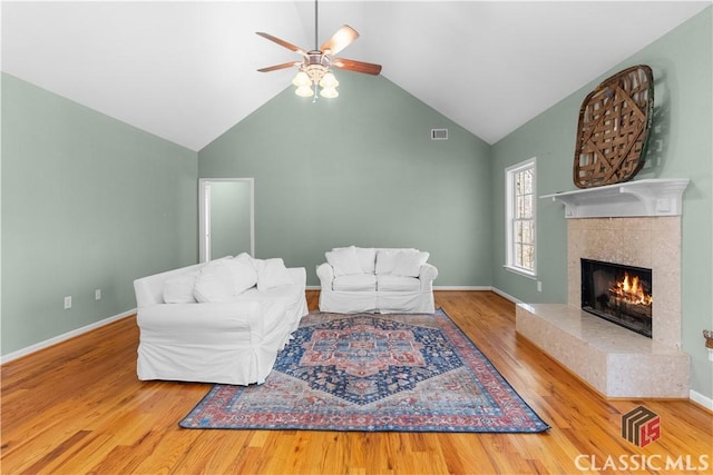 living area with visible vents, a ceiling fan, a tiled fireplace, wood finished floors, and baseboards