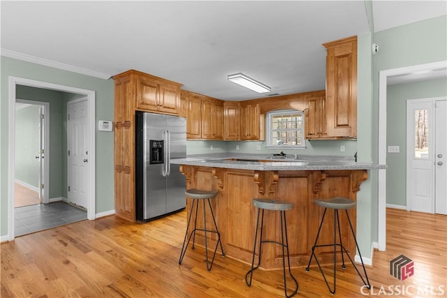 kitchen with light stone counters, a peninsula, stainless steel refrigerator with ice dispenser, a kitchen breakfast bar, and light wood-type flooring