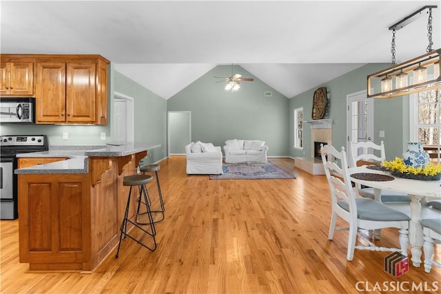 kitchen with a breakfast bar area, a ceiling fan, brown cabinets, stainless steel appliances, and open floor plan