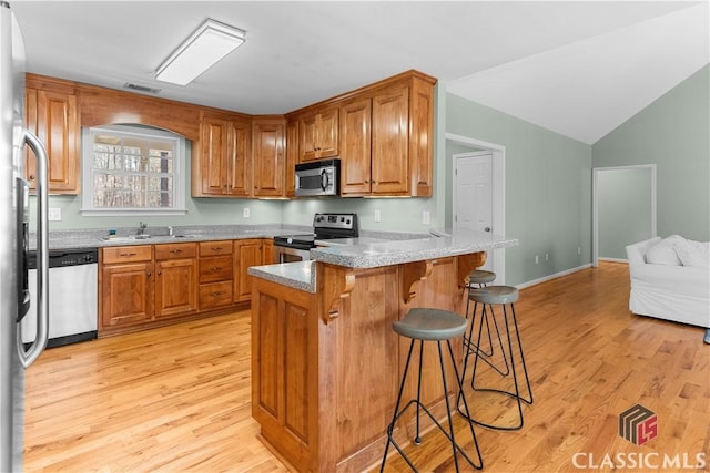 kitchen with stainless steel appliances, a peninsula, a breakfast bar area, and brown cabinetry