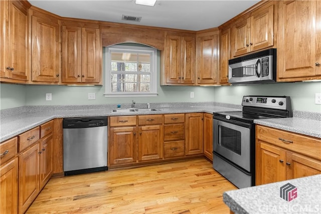 kitchen with light wood finished floors, visible vents, brown cabinets, appliances with stainless steel finishes, and a sink