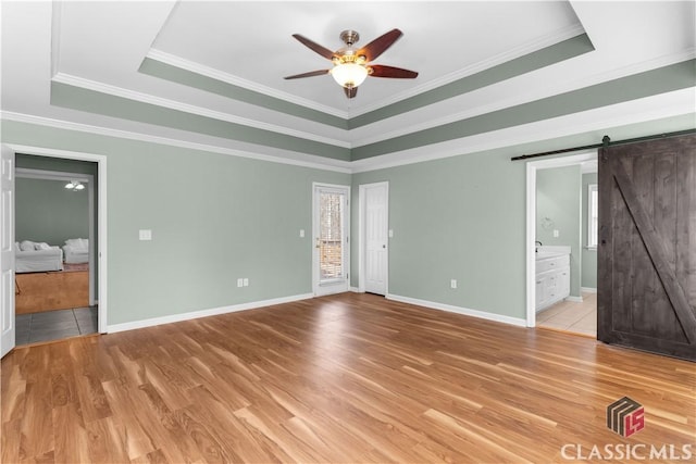 unfurnished bedroom with light wood-type flooring, a barn door, a raised ceiling, and ornamental molding