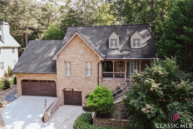 new england style home with stairway, roof with shingles, covered porch, concrete driveway, and stone siding