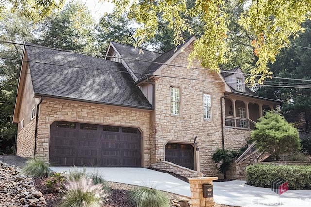 view of front of house featuring stone siding, stairway, roof with shingles, concrete driveway, and an attached garage