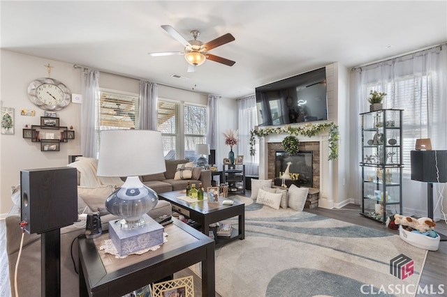 living area featuring visible vents, a ceiling fan, a glass covered fireplace, wood finished floors, and baseboards