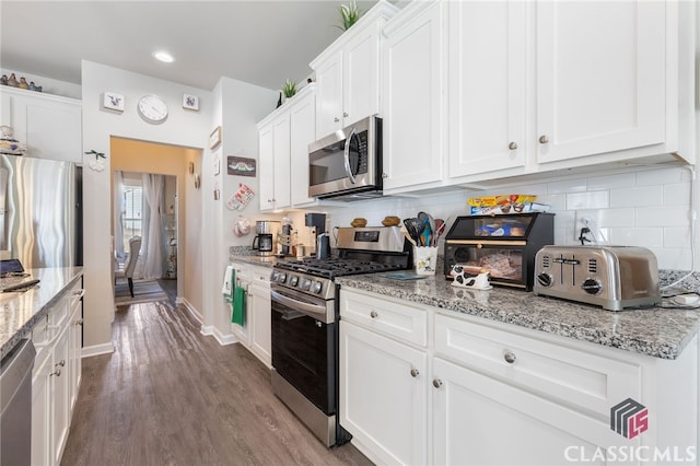 kitchen with tasteful backsplash, white cabinets, appliances with stainless steel finishes, and wood finished floors