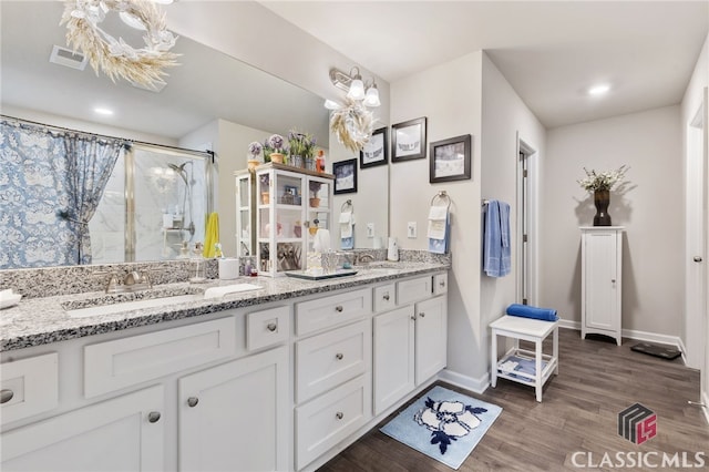 full bathroom featuring a shower with shower curtain, wood finished floors, visible vents, double vanity, and a sink