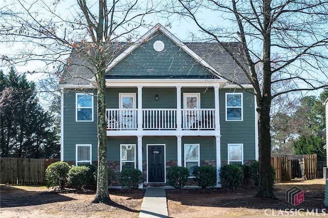 view of front facade with stone siding, a balcony, covered porch, and fence