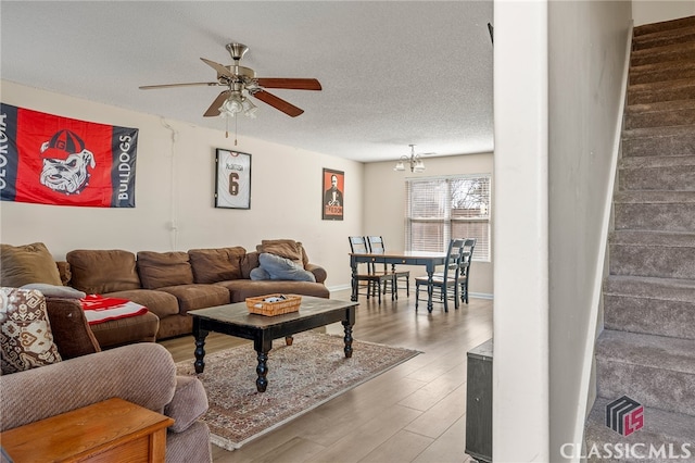 living room with a textured ceiling, wood finished floors, baseboards, ceiling fan, and stairs